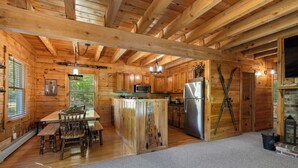A log cabin interior with a wooden dining table, chairs, a kitchen with a refrigerator and microwave, and a fireplace. - Cozy authentic log cabin with hot tub, Lake Access, near Sunday River & Mt Abram (Greenwood)