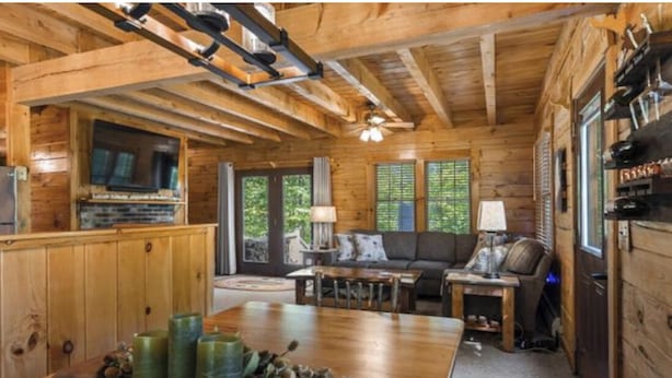A wooden cabin interior with a dining area, sofa, and a television. - Cozy authentic log cabin with hot tub, Lake Access, near Sunday River & Mt Abram (Greenwood)
