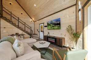 Un intérieur en bois comprenant un canapé, une table basse, une cheminée, un téléviseur et un escalier.