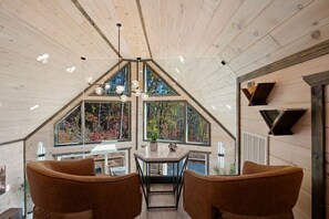 A room with a sloped ceiling, large windows, a table with chairs, and a hanging light fixture. - Cozy cabin w/ theatre, game room & hot tub (Sevierville)