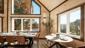 Un comedor con techo alto, ventanas grandes y vistas a árboles otoñales.