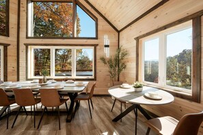 A dining area with a high ceiling, large windows, and a view of autumn trees. - Cozy cabin w/ theatre, game room & hot tub (Sevierville)
