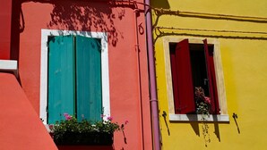 A building with two windows, one with teal shutters and one with red shutters, and a small balcony with flowers. - Bright Property Close to Ponente Beach (Caorle)