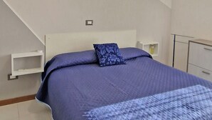 A bedroom with a bed, a nightstand, a lamp, and a small shelf. - Bright Property Close to Ponente Beach (Caorle)
