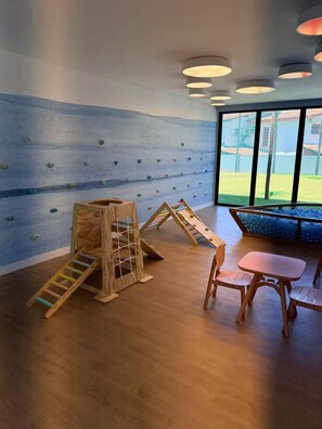 A play area with climbing walls and a slide, a small table with chairs, and a view through large windows. - Flat 003 | Studio Garden with pool views (Tamandaré)