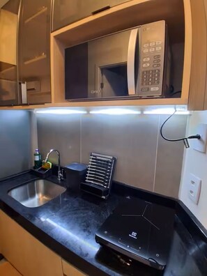 A modern kitchen with a built-in microwave, a stainless steel sink, and a black countertop. - Flat 003 | Studio Garden with pool views (Tamandaré)