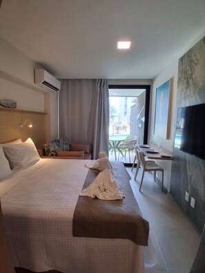 Quarto de hotel com cama, escrivaninha, cadeira, televisão e varanda com vista.