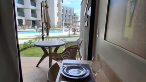 Ein Essbereich mit einem Tisch für zwei Personen, Blick auf den Pool und ein Gebäude im Hintergrund.