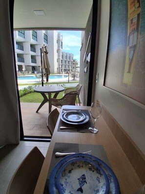 Uma área de refeições com uma mesa posta para dois, vista para a piscina e um edifício ao fundo.