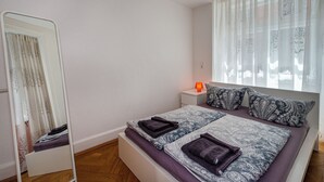 Una camera da letto con un letto, un comodino, uno specchio e una finestra con tende leggere.