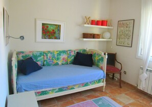 A room with a floral-patterned sofa, a chair, a shelf with baskets and a framed alphabet chart, and a radiator.