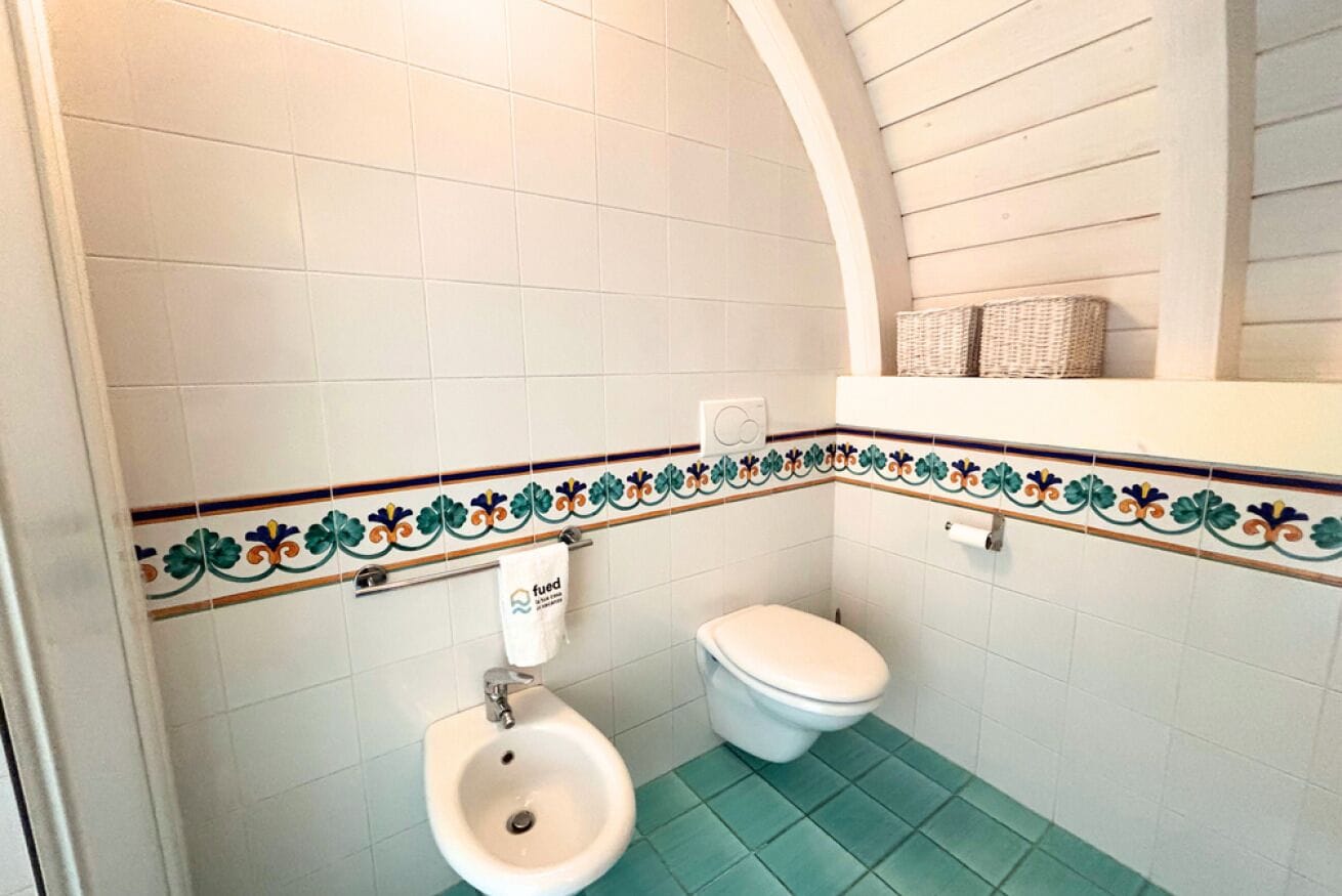 Une salle de bain avec des toilettes blanches, un lavabo et une bordure décorative en carreaux.