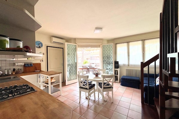 Une cuisine avec un coin repas, un escalier et une vue sur l’extérieur, visible à travers une porte vitrée.
