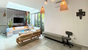 Una sala de estar moderna con un sofá, un banco, un televisor y un ventanal grande.