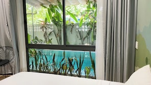 Ein Zimmer mit einem Bett, einem Fenster mit Blick auf einen Pool und Pflanzen sowie einem Sessel.