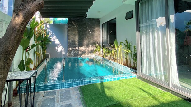 Un área de piscina moderna al aire libre con borde de azulejos, pared de piedra y puerta de vidrio que da a un porche cubierto.
