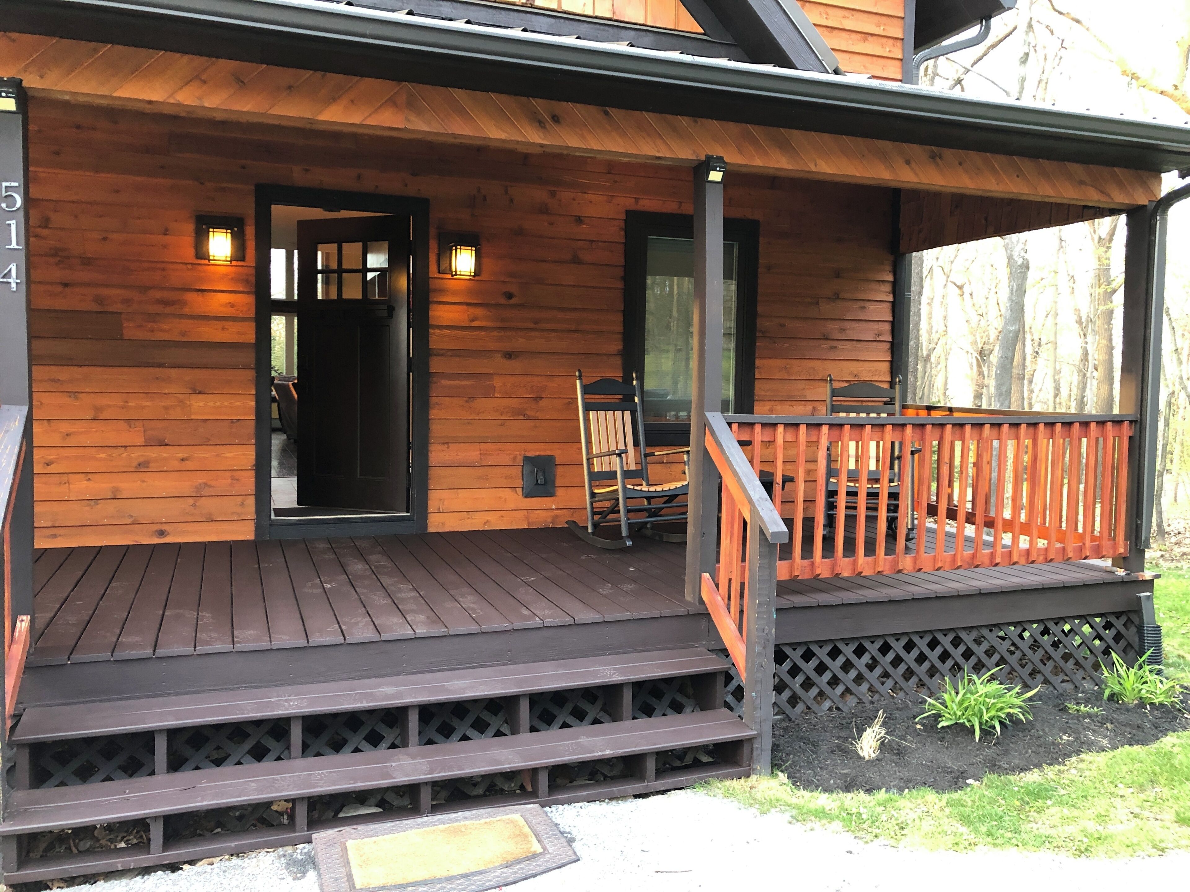 Une cabane en bois avec un porche, une porte et un petit espace extérieur aménagé pour s’asseoir.