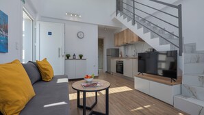 A modern living space with a sofa, a dining table, a kitchen area, and a staircase. - SLV Irida Apartment (Pangaio)