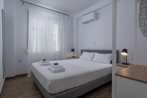 Et rent, moderne hotelværelse med seng, hvide gardiner, en aircondition, en senget lampe og et natbord i træ.