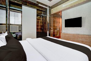 A modern hotel room with a large bed, a TV mounted on the wall, and a glass door leading to a bathroom.