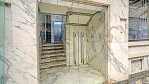 Uma entrada de mármore com portas de vidro e uma escadaria que leva ao interior.