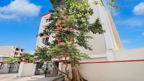 A multi-story building with a white facade and red trim, a tree in front, and a clear blue sky. - Premiumcollection O Bhanugudi Junction (Kakinada)