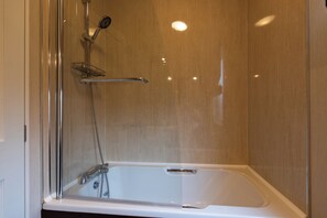 A glass-enclosed shower with a handheld showerhead and a handheld faucet.