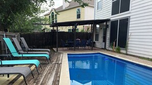 Un jardin avec une piscine, une terrasse en bois et des chaises longues.