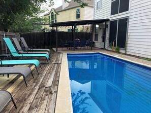 Ein Garten mit Schwimmbad, Holzterrasse und Liegestühlen.