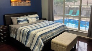 Une chambre à coucher avec un lit, une table de chevet, une fenêtre donnant sur une piscine et un tableau accroché au mur.