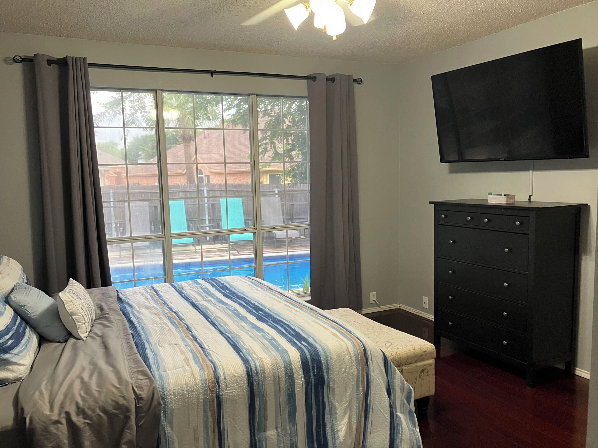 A bedroom with a bed, a dresser, a television, and a view of a swimming pool.