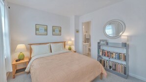Quarto com cama, abajures, estante de livros e espelho.