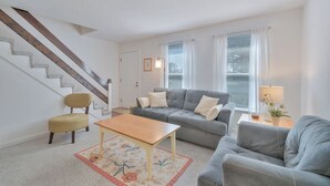 Sala de estar com escada, sofá cinza, mesa de centro de madeira e poltrona amarela.