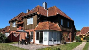 A two-story house with a patio, a covered outdoor seating area, and a visible chimney. - Ferienwohnung in Petersdorf auf Fehmarn (Fehmarn)