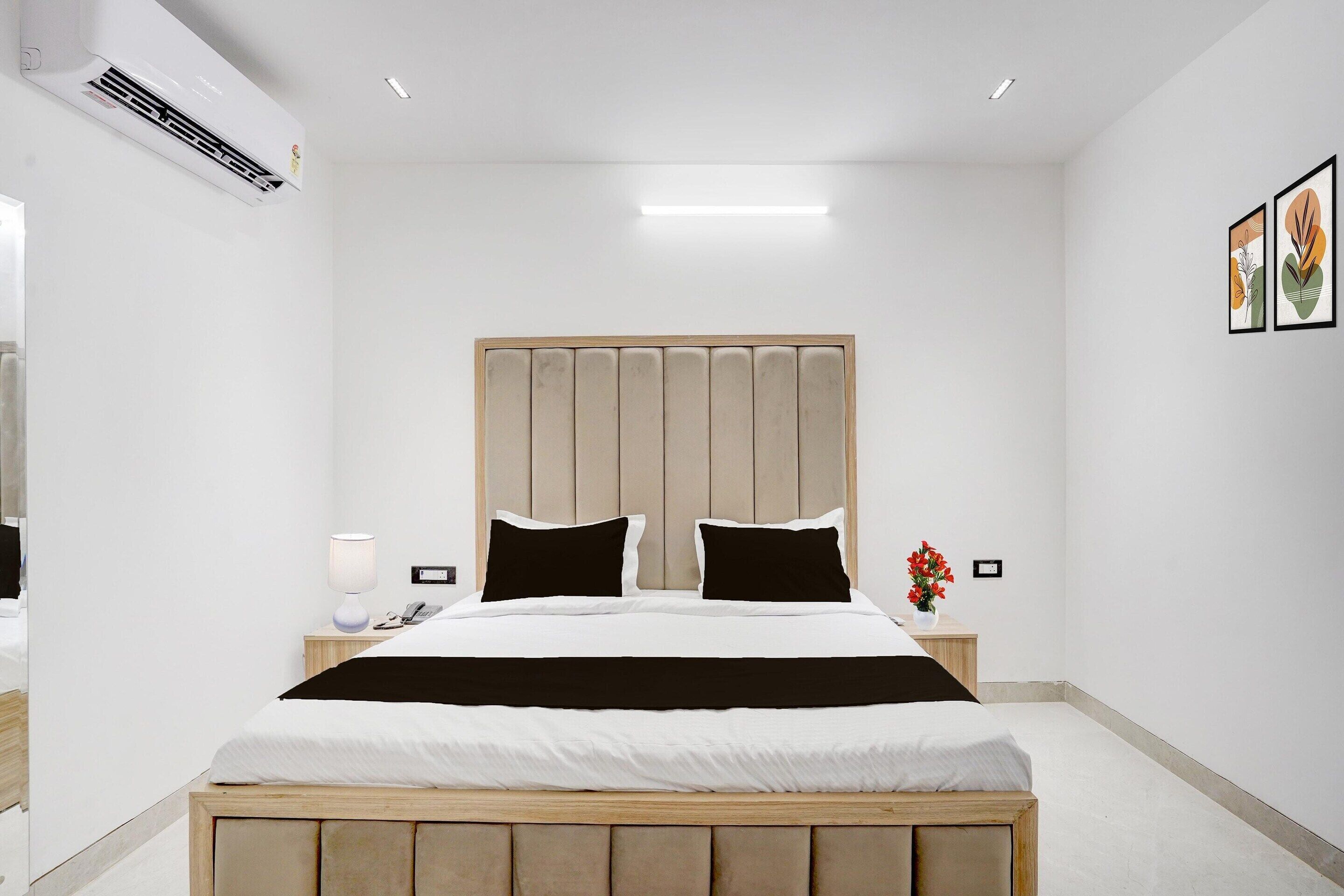 A hotel room with a bed, bedside table, lamp, and artwork on the wall.