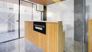 Vastaanottotiski, jossa on kyltti, jossa lukee ”TOWNHOUSE”, ja jossa on yrityksen logo, sekä puupanelointi ja lasiseinä.