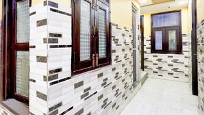 A hallway with tiled walls and a tiled floor, leading to a door with a window. - Saver Doublehotel Welcome Inn (New Delhi)
