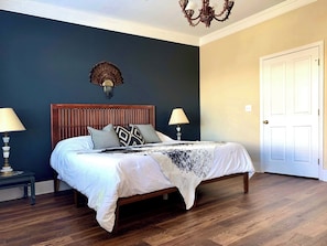 Un dormitorio con una cama de madera, dos lámparas de noche, una pared oscura, una puerta blanca y un candelabro.