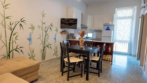 Una cocina moderna con armarios blancos, una mesa de comedor con sillas, un televisor montado sobre la encimera y un jarrón decorativo en la mesa.