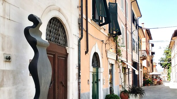 Una calle con edificios, una escultura y una puerta con la leyenda 'DAPHNIE'.