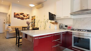 Una cocina moderna con una isla roja, armarios blancos, horno empotrado y un comedor con sofá y sillas.