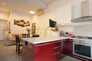 Une cuisine moderne avec un îlot central rouge, des armoires blanches, un four encastré et un coin repas comprenant un canapé et des chaises.