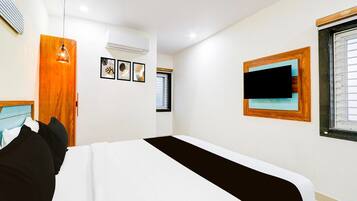 A hotel room with a bed, a wooden door, a wall-mounted TV, and a window with blinds.