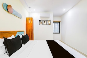 A hotel room with a bed, a wooden headboard, a wall-mounted artwork, a window with blinds, and an air conditioning unit.