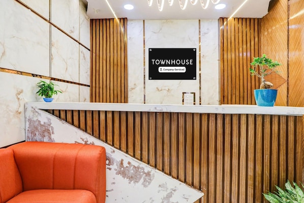 A reception area with a 'TOWNHOUSE' sign, a reception desk, a wooden slatted wall, a potted plant, and a red chair.