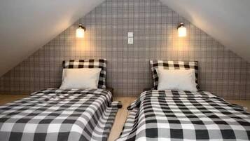 A room with two beds, checkered bedding, a sloped ceiling, and wall-mounted lights.