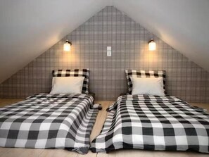 Ein Zimmer mit zwei Betten, karierten Bettbezügen, einer geneigten Decke und Wandleuchten.