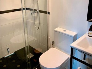 A bathroom with a glass shower enclosure, a white toilet, and a sink with a bottle of hand soap. - Holiday Cottages by the sea in an Oasis of Peace (Smoldzino)