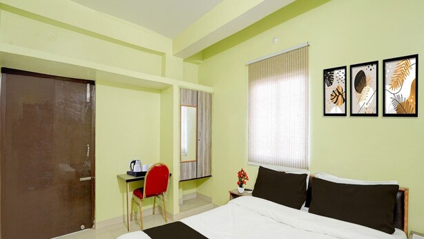 Habitación de hotel con una cama, un escritorio con una silla, una ventana con persianas y tres cuadros en la pared.