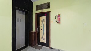 Un pasillo con un extintor fijado en la pared, una puerta con placa de número y un contenedor de basura.
